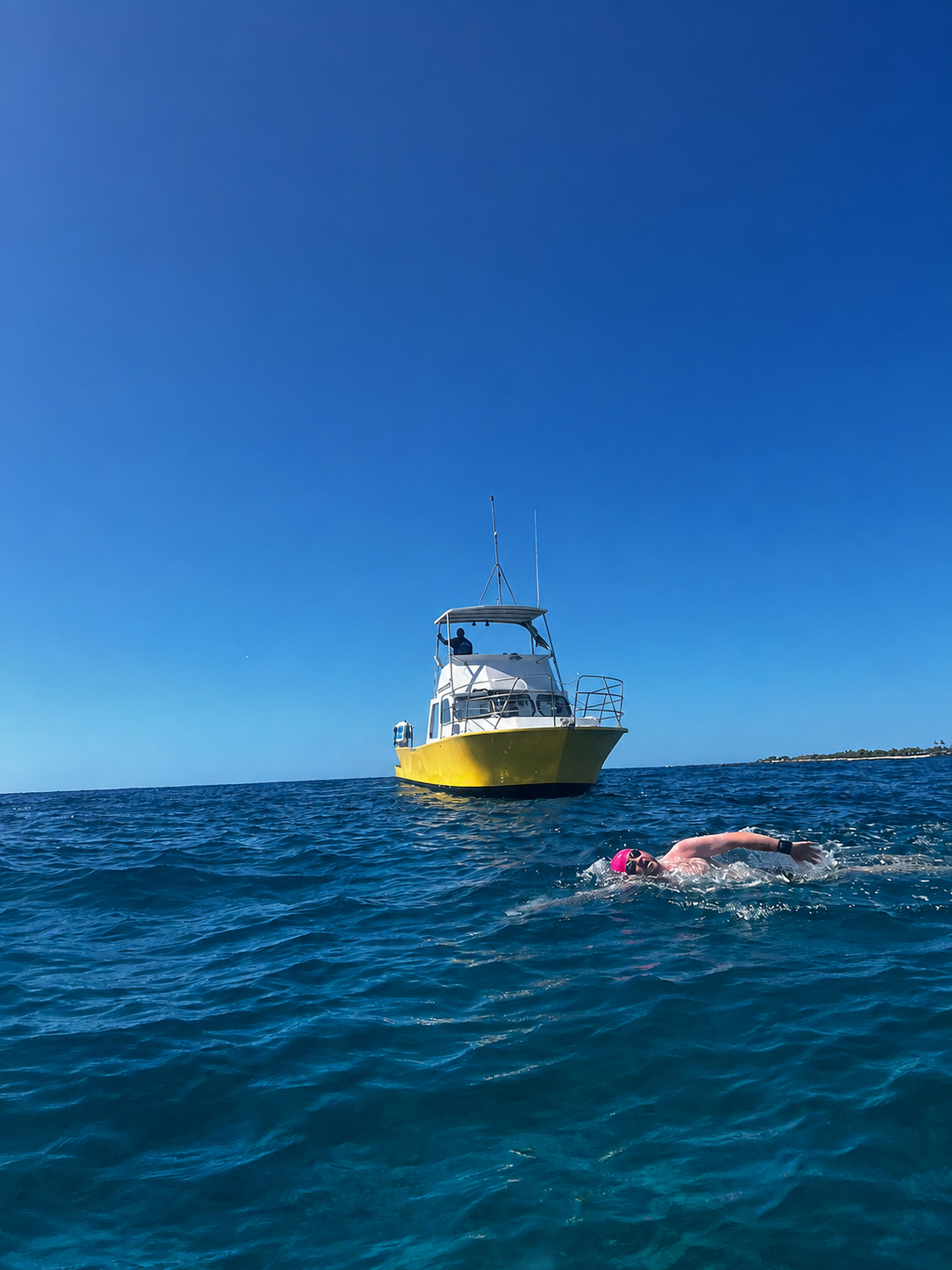 Greg swimming in open water with a support boat behind him